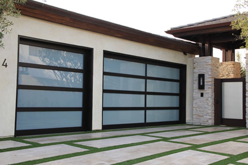 Modern glass-paneled garage doors on a contemporary stucco home with stone walkway