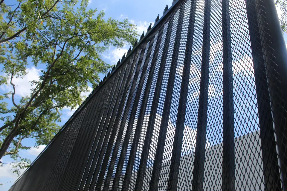 Tall black chain-link fence with privacy slats installed along a commercial property line under a blue sky