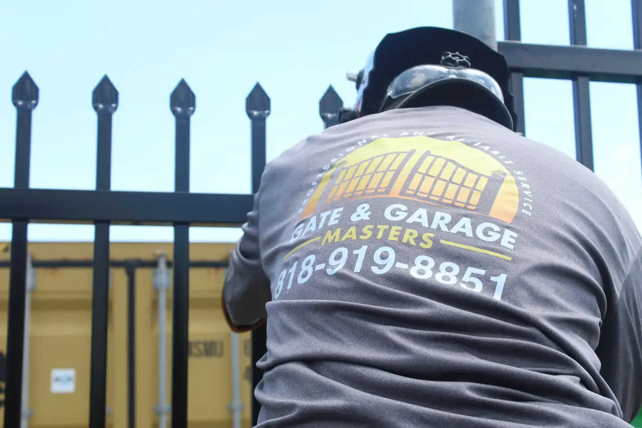 Gate & Garage Masters technician in branded uniform inspecting a black iron gate