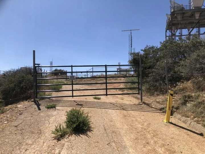 Open rail gate at an unpaved property approach.