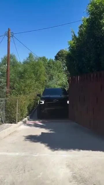 Film still: timber driveway gate opening for vehicle access.